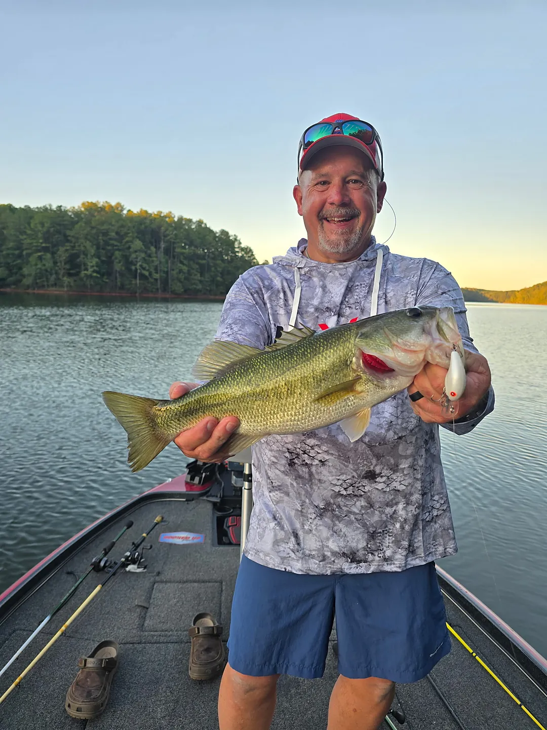 A grinning angler on the front deck holding up a largemouth bass that hit a white crankbait