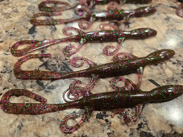 Four soft plastic lizards in a brown and pink with green and purple flake, curly legs and long tails